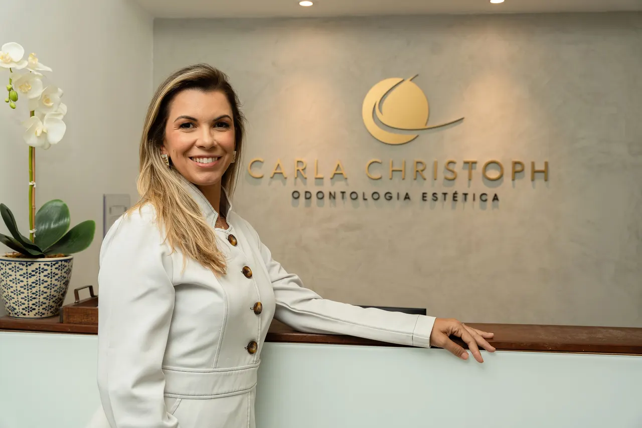 Dra. Carla Christoph na recepção do consultório em Ipanema, com o logo da clínica ao fundo
